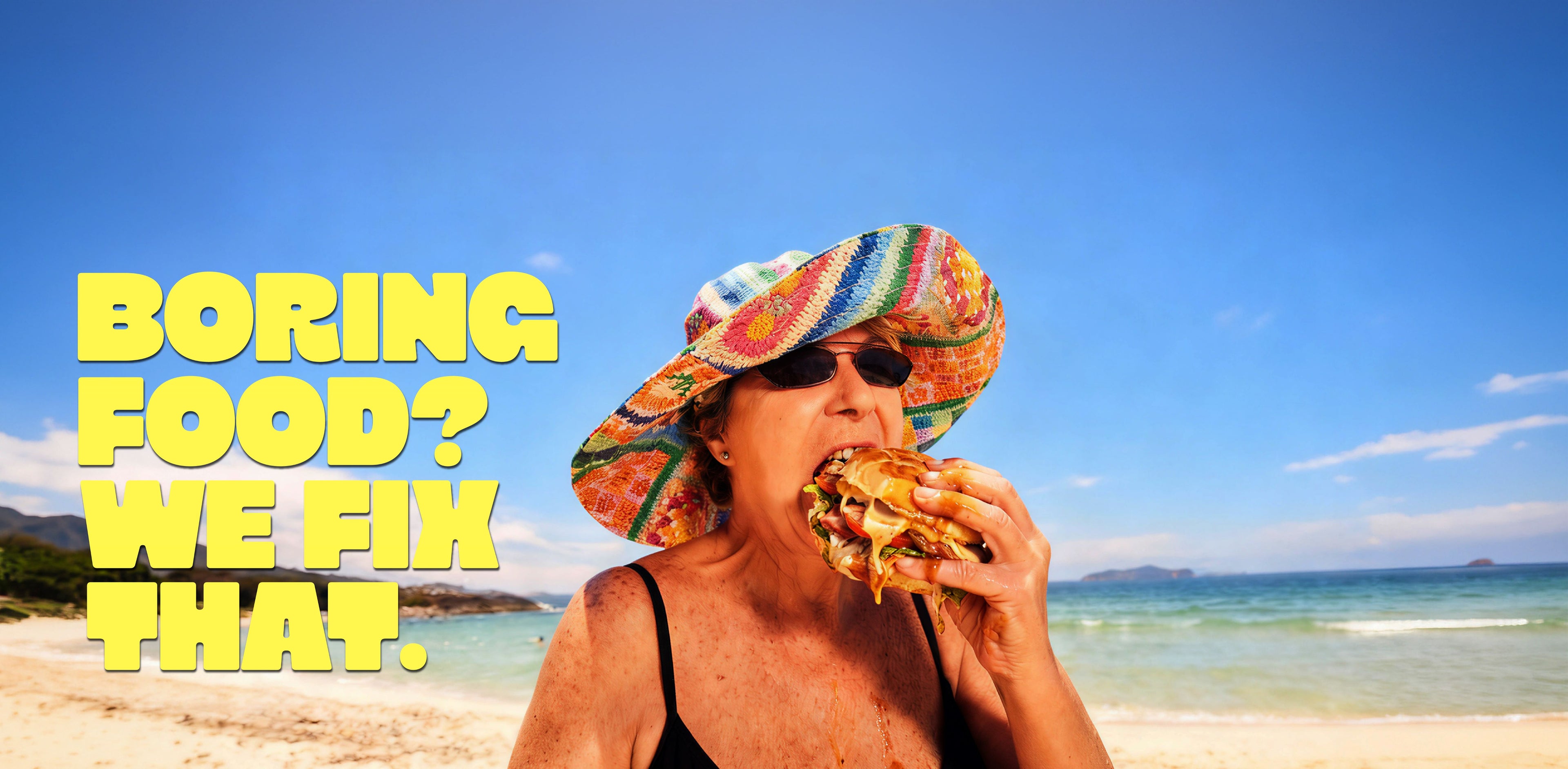 A woman on a beach wearing a colorful patterned sun hat and sunglasses, eating a large sandwich. Large yellow text on the left reads, 'BORING FOOD? WE FIX THAT.